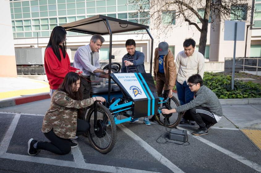 教师 mentor and students working on a solar-powered bicycle.
